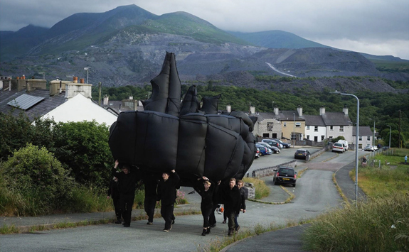 A group of men carrying inflatable sculpture up a hill
